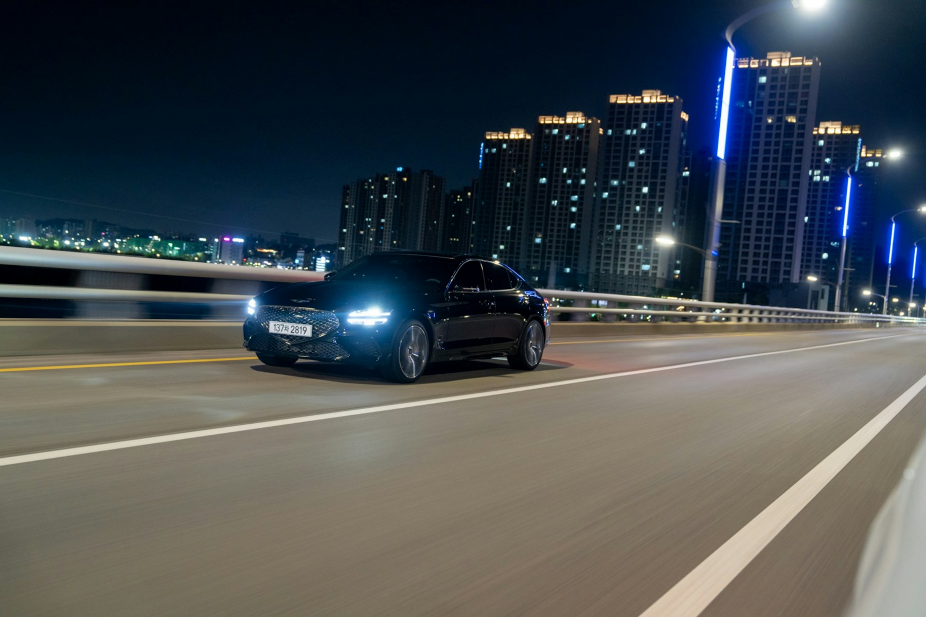 A dark executive sedan moving through a city at night under streetlight
